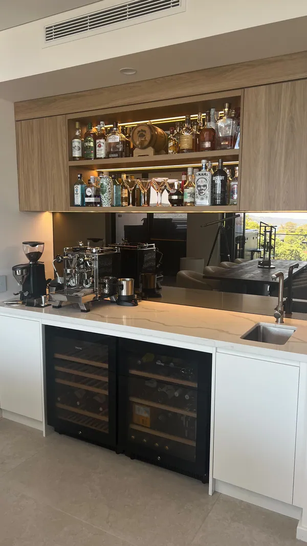Bronze mirrored splashback behind a home bar with timber shelves and a coffee machine