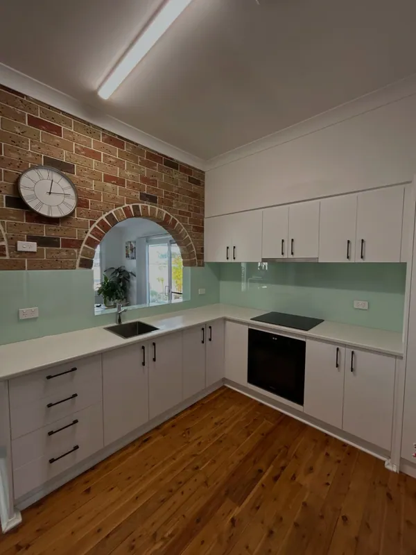 Green glass kitchen splashback beneath white cupboards and an arched wall opening
